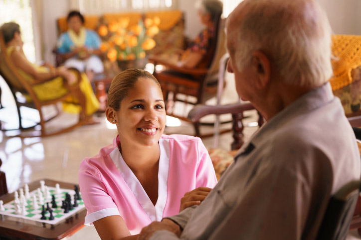 A nurse checks on a patient sitting in the game room at a long-term care facility in Spring Lake, LA