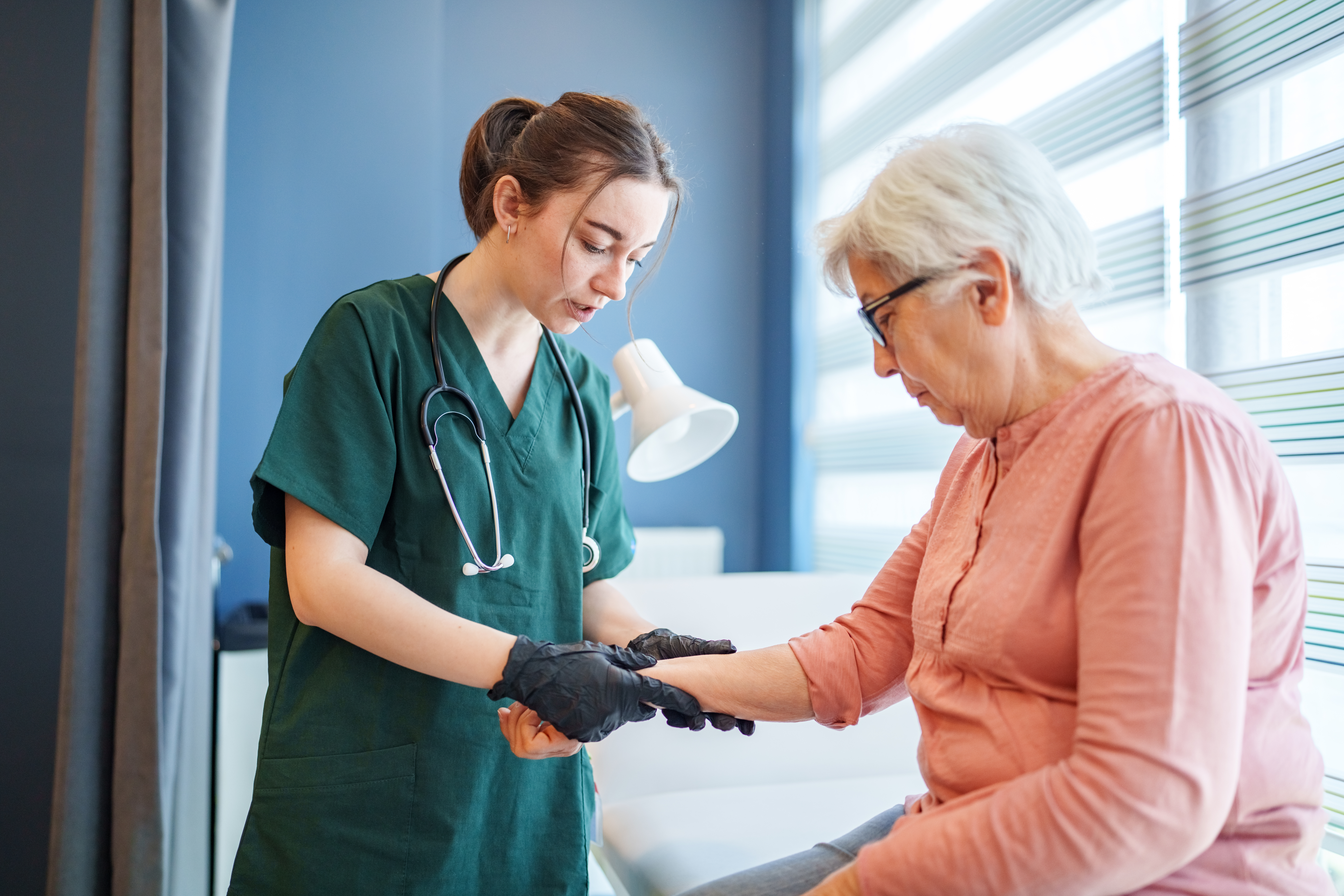 Doctor Wearing Medical Gloves While Performing Physical Examination on Elderly Patient in Clinic